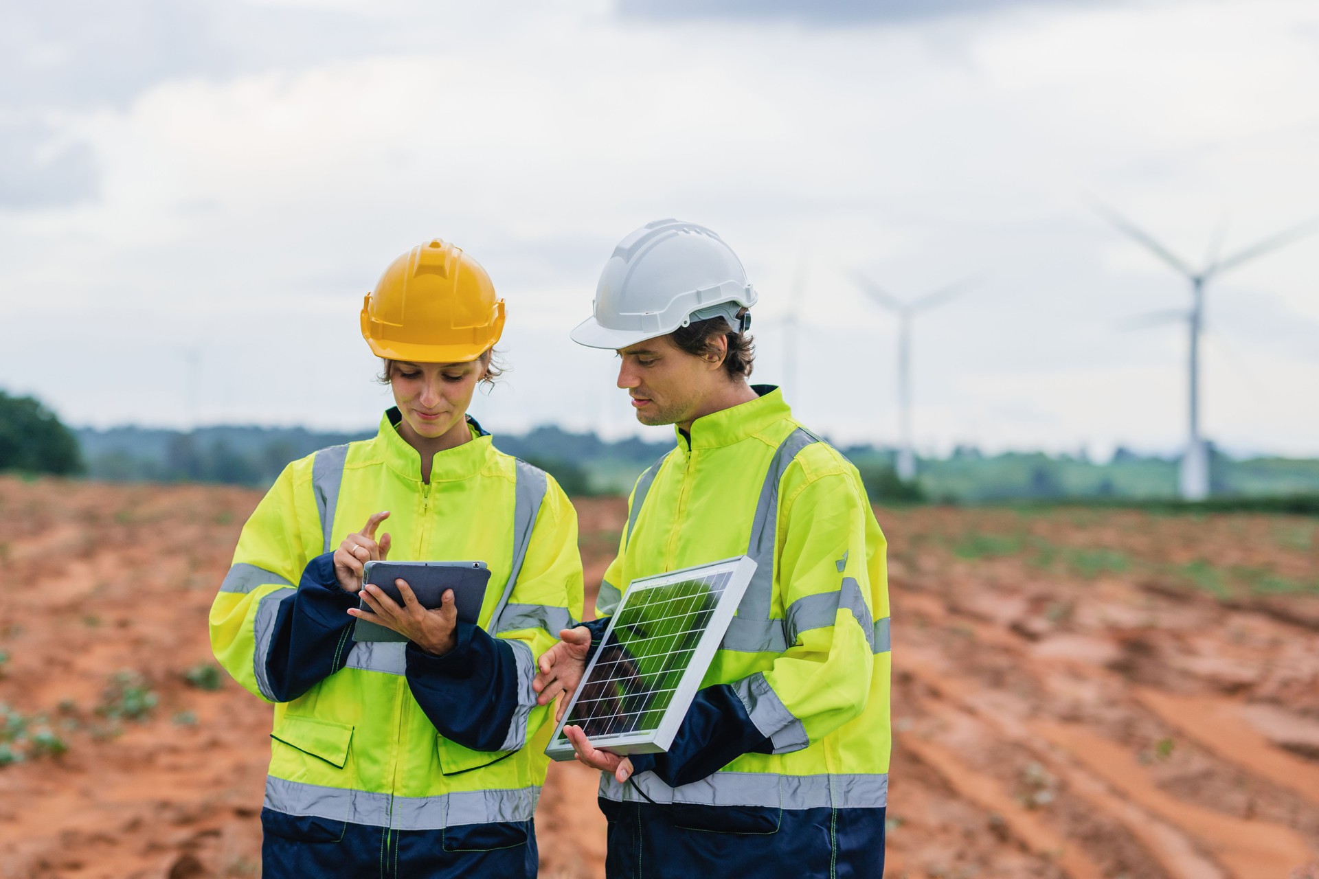 Two workers in yellow and white safety gear are looking at a tablet